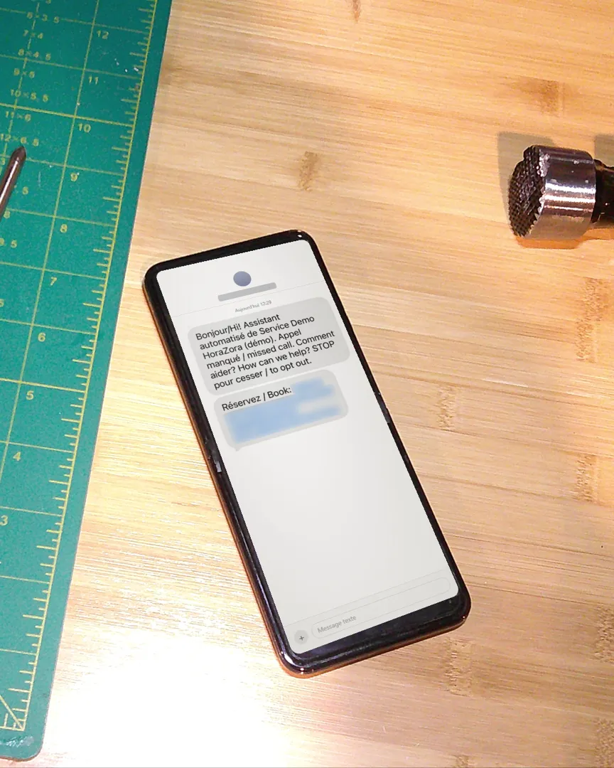 Un téléphone sur un établi affichant le texto automatique de la démo HoraZora après un appel manqué, avec un lien de réservation.